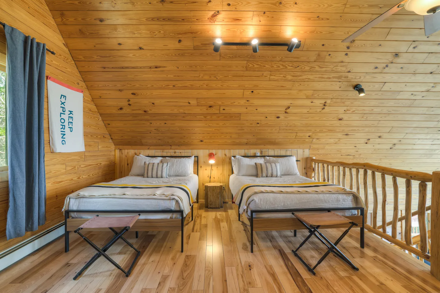 Loft bedroom with wood paneled walls and ceiling, featuring two twin beds side by side on hardwood flooring.