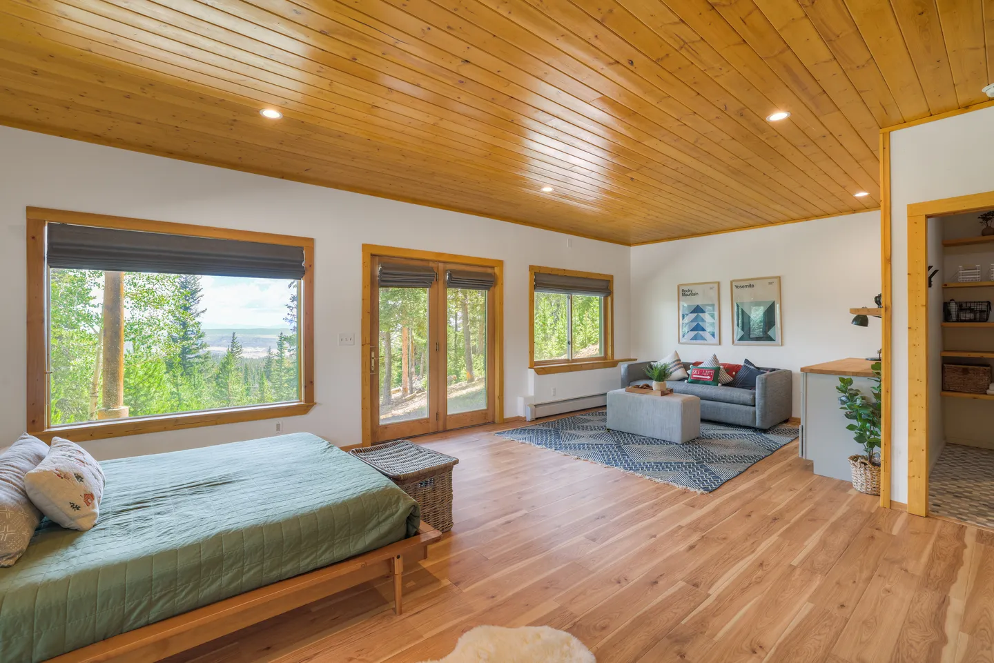 Spacious bedroom suite featuring a wood-plank ceiling, wood floors, a bed with a green coverlet, and a sitting area with a sofa.
