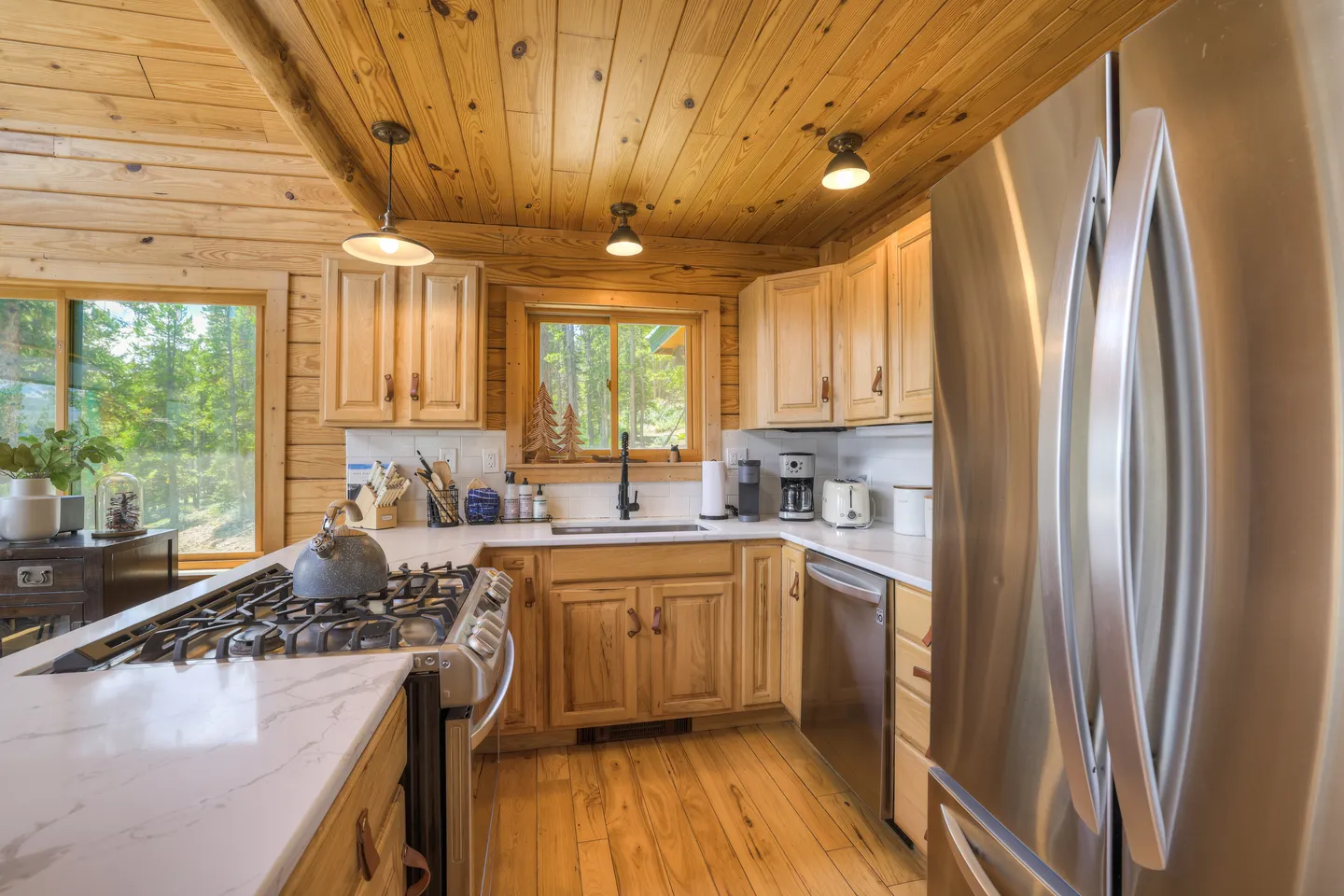 Kitchen with wooden cabinetry, stainless steel appliances, marble-look countertops, and wood-paneled walls and ceiling.