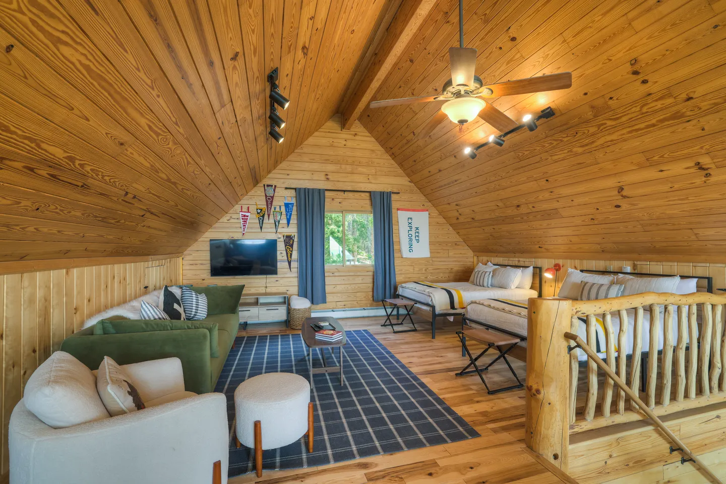 Loft bedroom and living area with wood-paneled walls and ceiling, two beds, a green sofa, and an armchair.