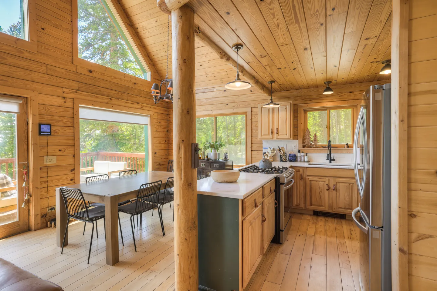 Open-concept cabin interior featuring an all-wood kitchen and adjacent dining area with large windows.
