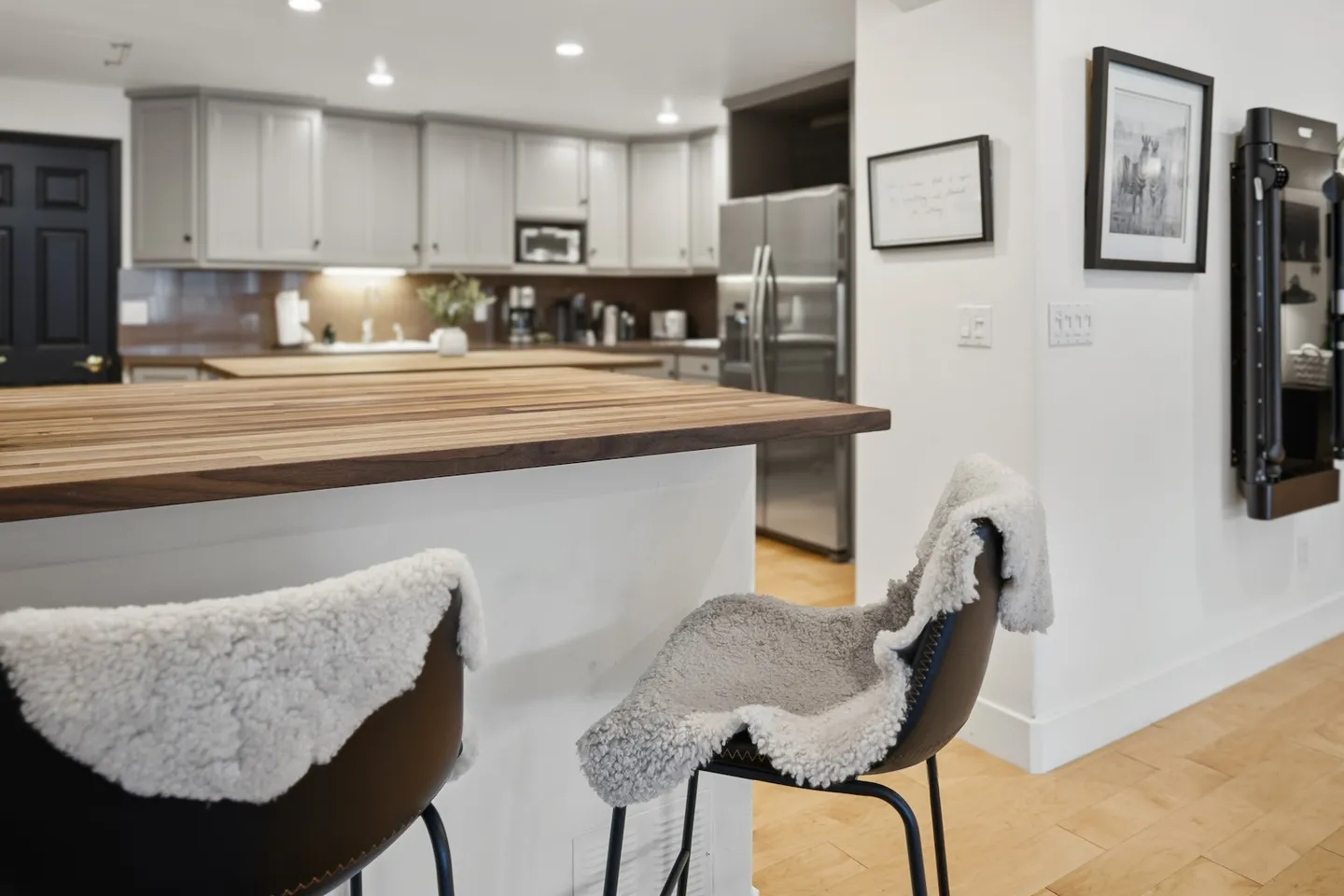 A kitchen island with a butcher block countertop and two barstools draped in fleece blankets, looking into the main kitchen area.
