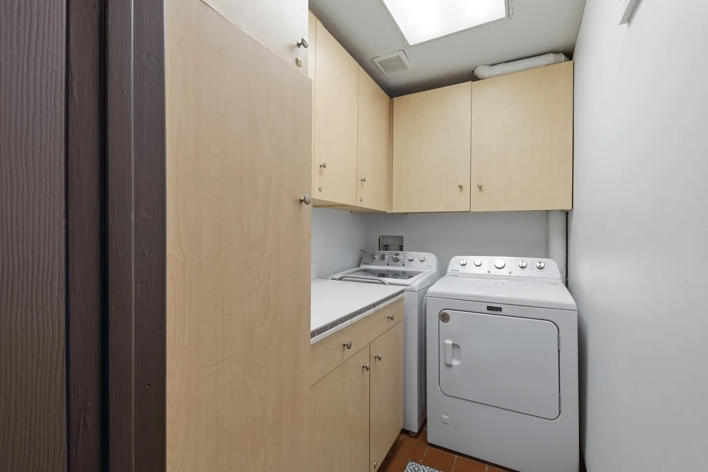 Dedicated indoor laundry room featuring a white washer and dryer, tiled countertop, and light wood cabinetry.