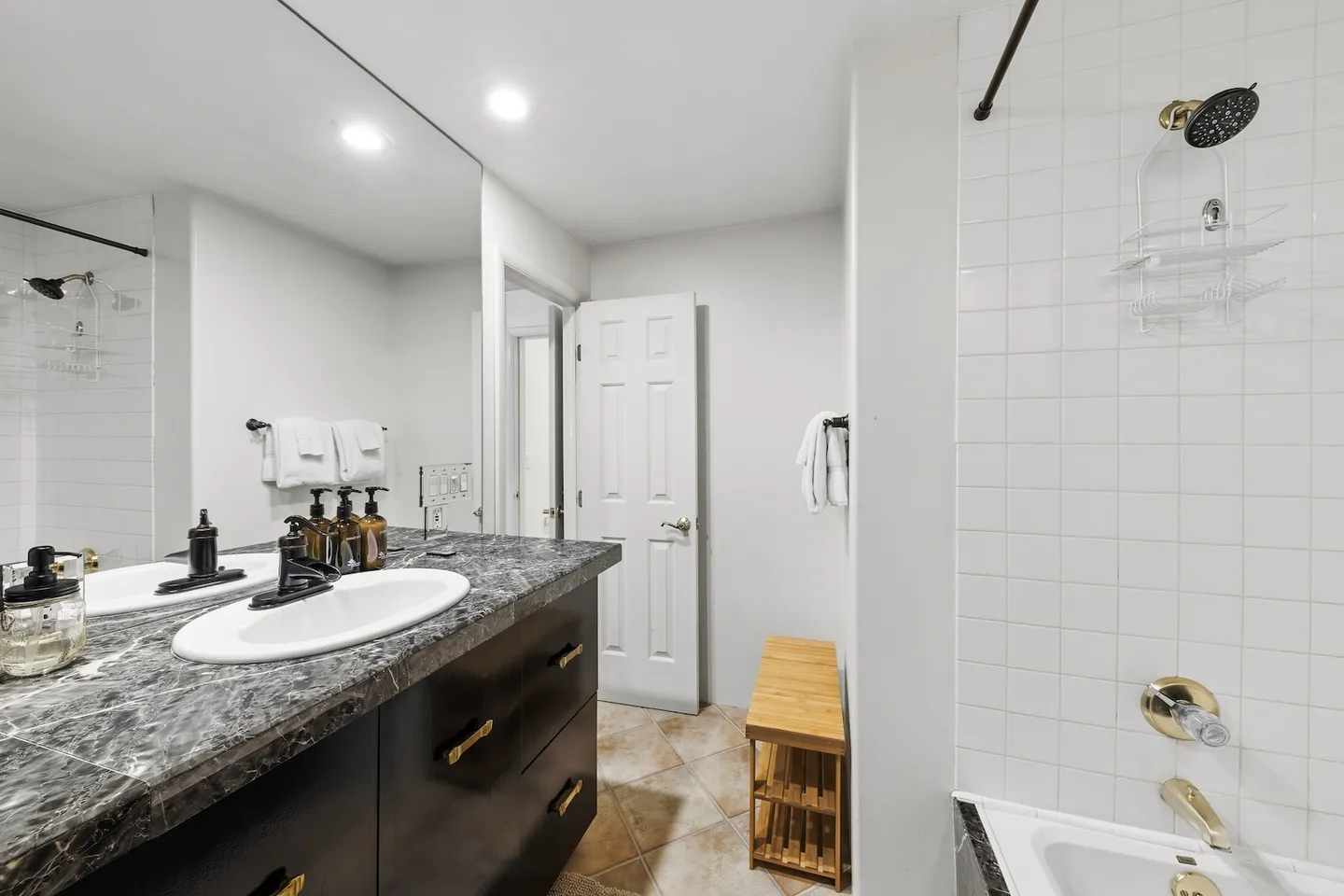 Bathroom featuring a dark vanity with a marble-style countertop, large mirror, and tiled shower and tub area with gold hardware.