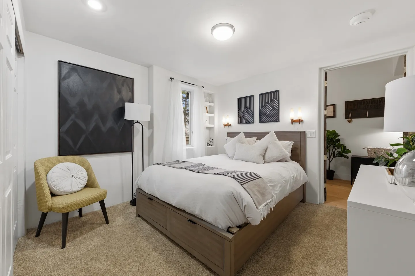Bedroom with a wood-frame bed with storage drawers, carpeted floor, yellow accent chair, and doorway to an adjacent room.