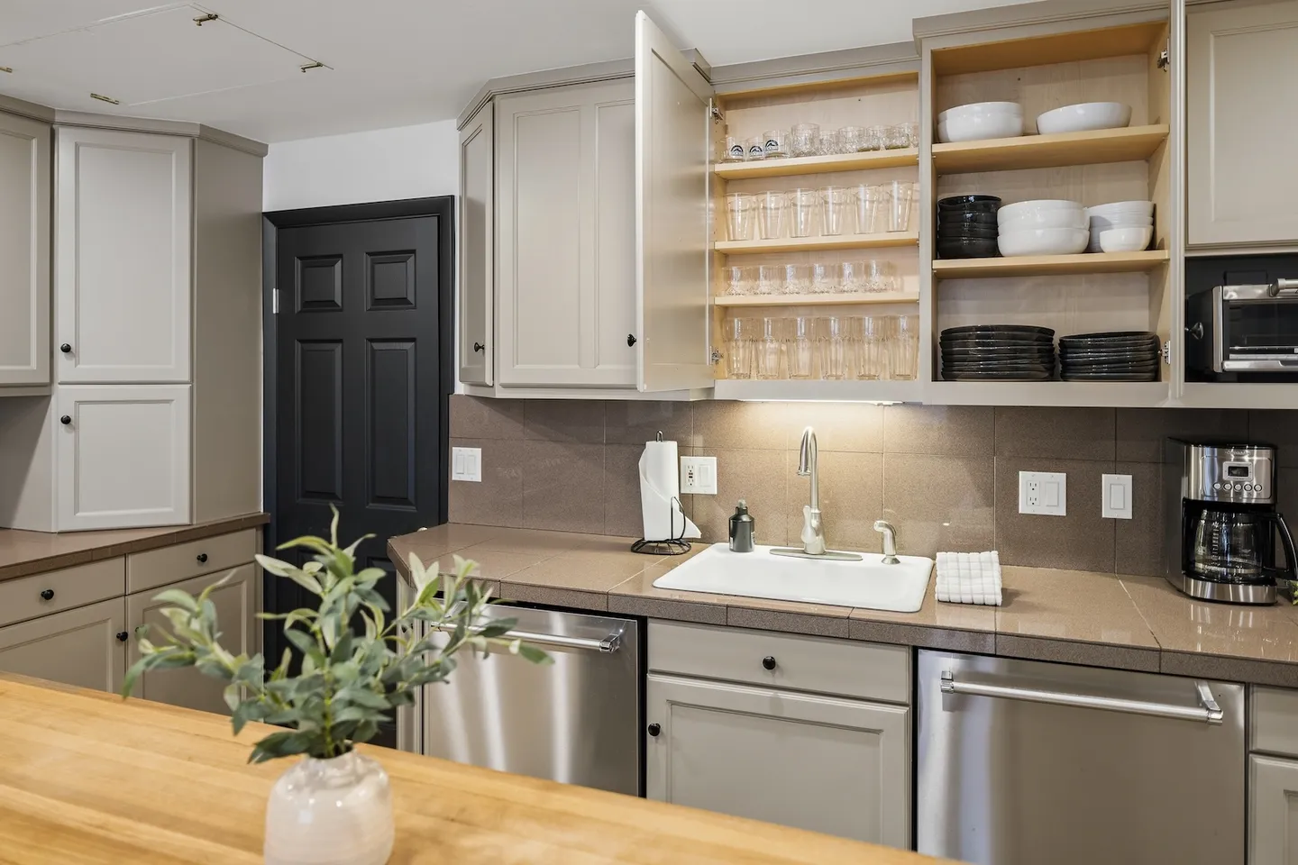 Kitchen counter and sink area with upper cabinets open showing glassware, bowls, and plates.