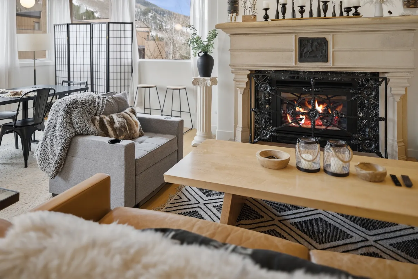 Living room featuring a glowing fireplace, a wood coffee table, comfortable seating, and windows with mountain views in the background.
