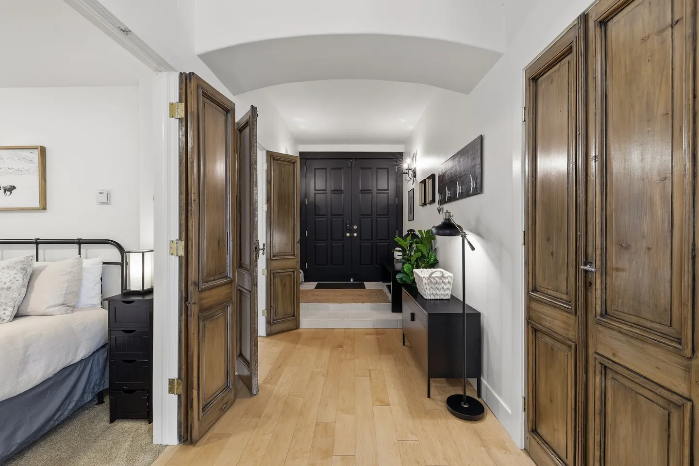 Hallway with wood floors and rustic paneled doors looking toward a black double front door.