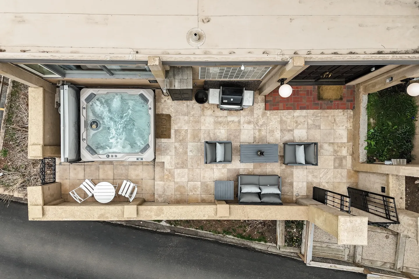 Top-down overhead view of an outdoor stone patio featuring a hot tub, outdoor seating set, and barbecue grill.
