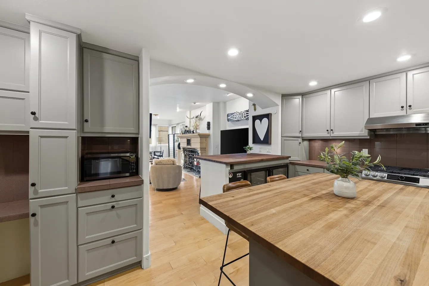 Kitchen with gray cabinetry, butcher block countertops, recessed lighting, and a view into the adjoining living room.