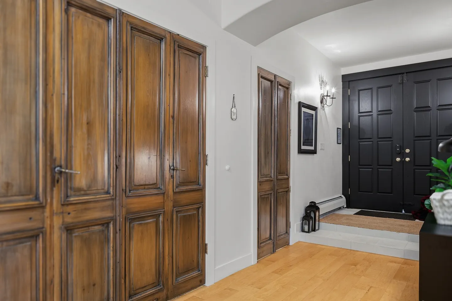 Entryway hallway showing wooden paneled interior doors, light-colored flooring, and a dark double front entrance door.