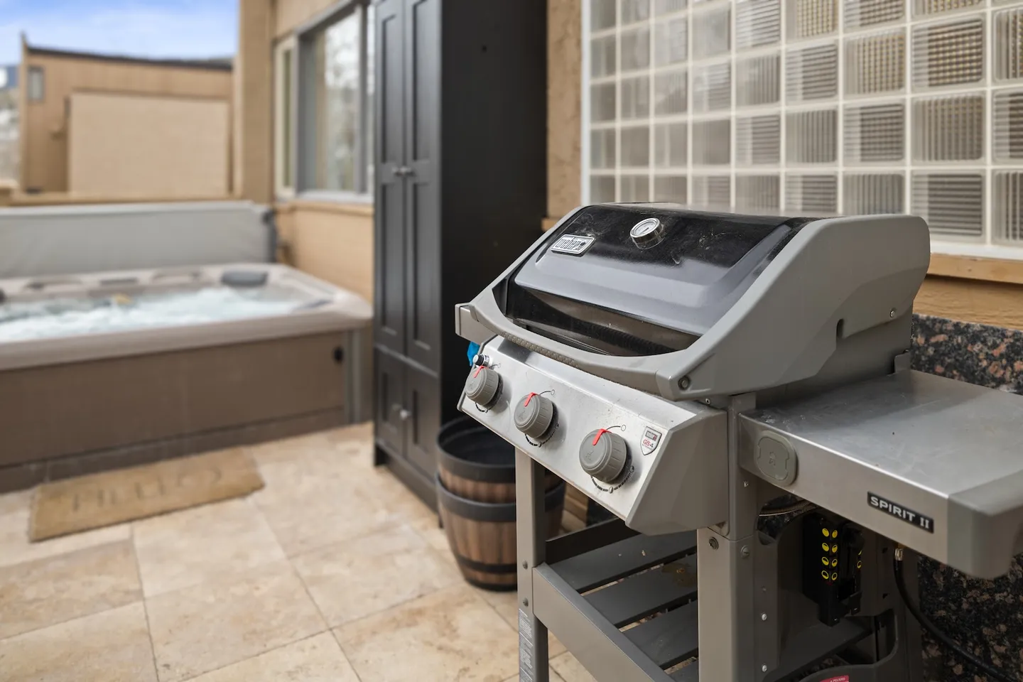 Outdoor patio with a barbecue grill in the foreground and a bubbling hot tub in the background.