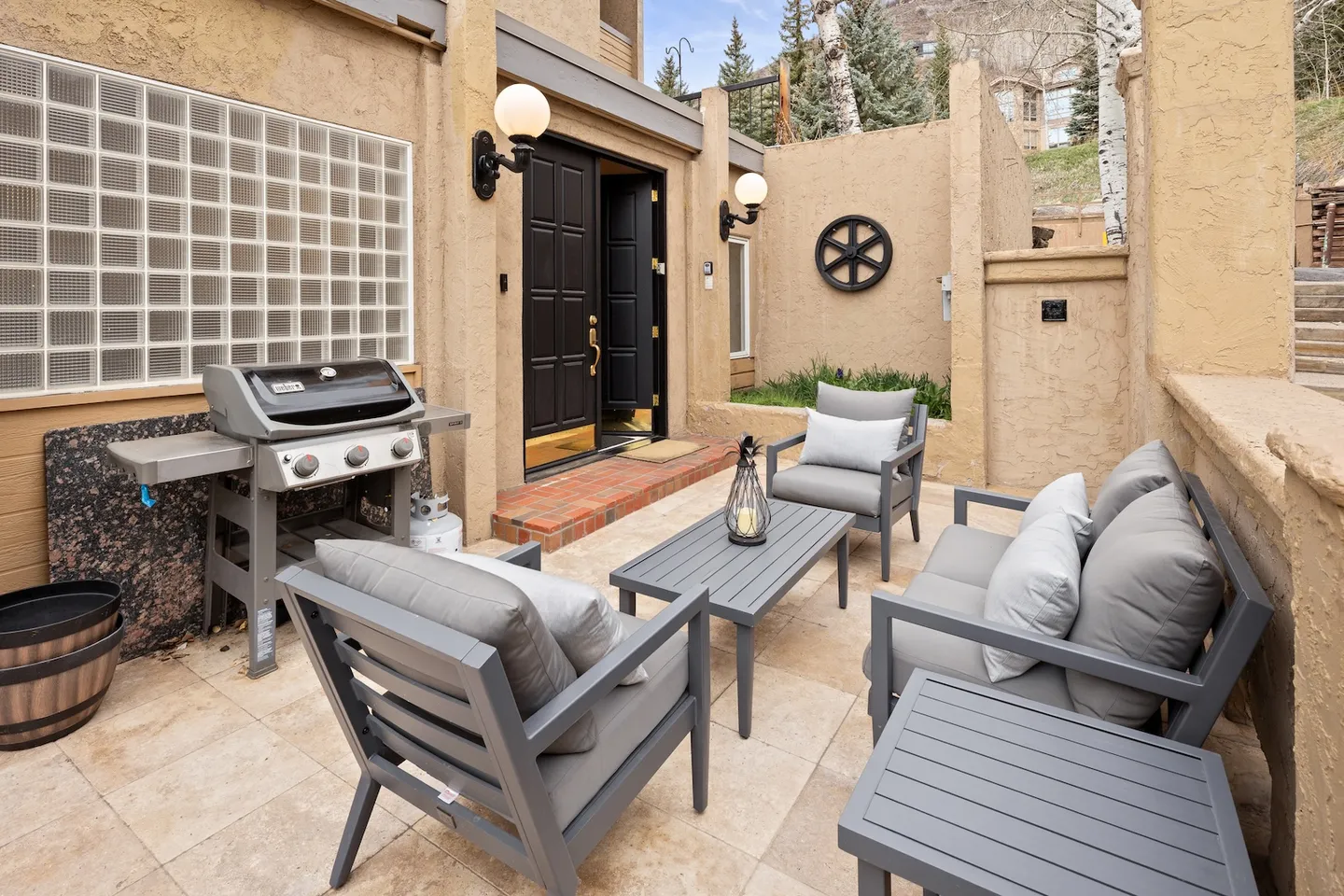 Outdoor paved patio entrance featuring a barbecue grill, grey cushioned seating set, coffee table, and the home's front door.
