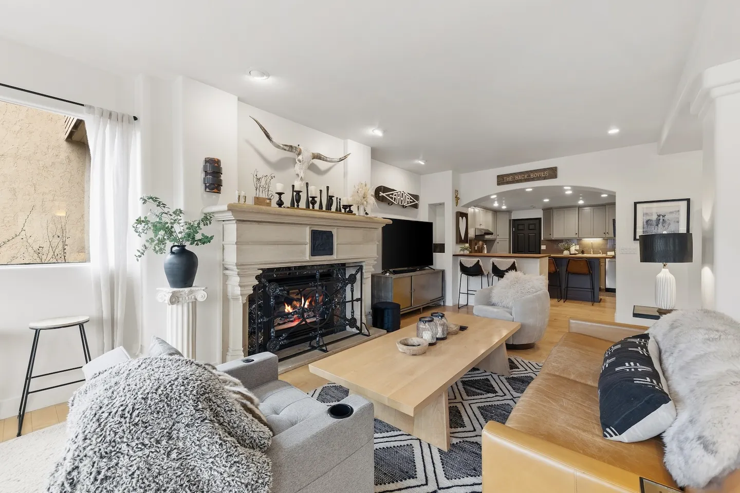 Living room with a large fireplace, seating area, and an arched view into the adjoining kitchen.