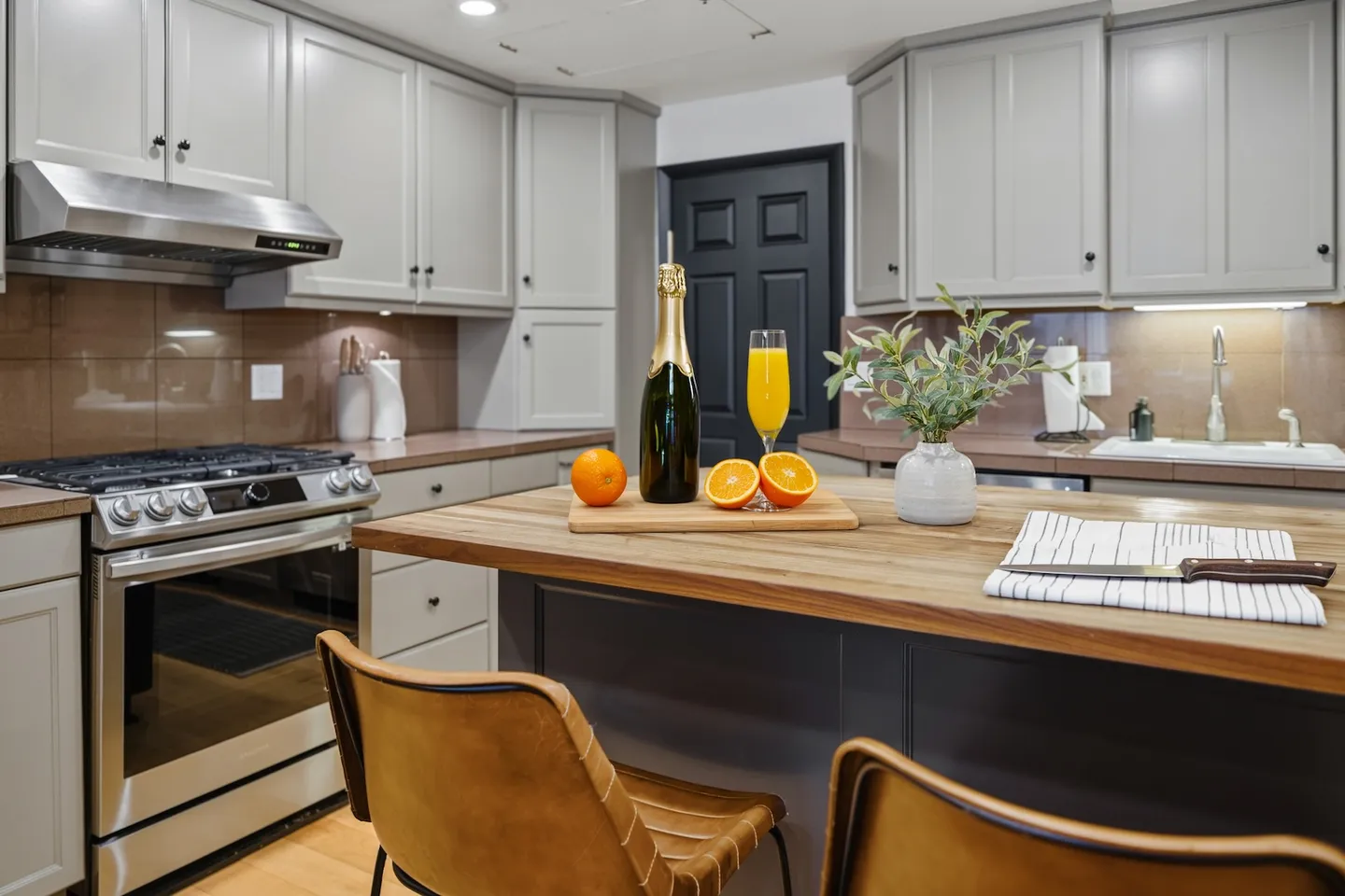 A kitchen featuring a wooden island with bar stools, stainless steel stove, and light gray cabinetry.