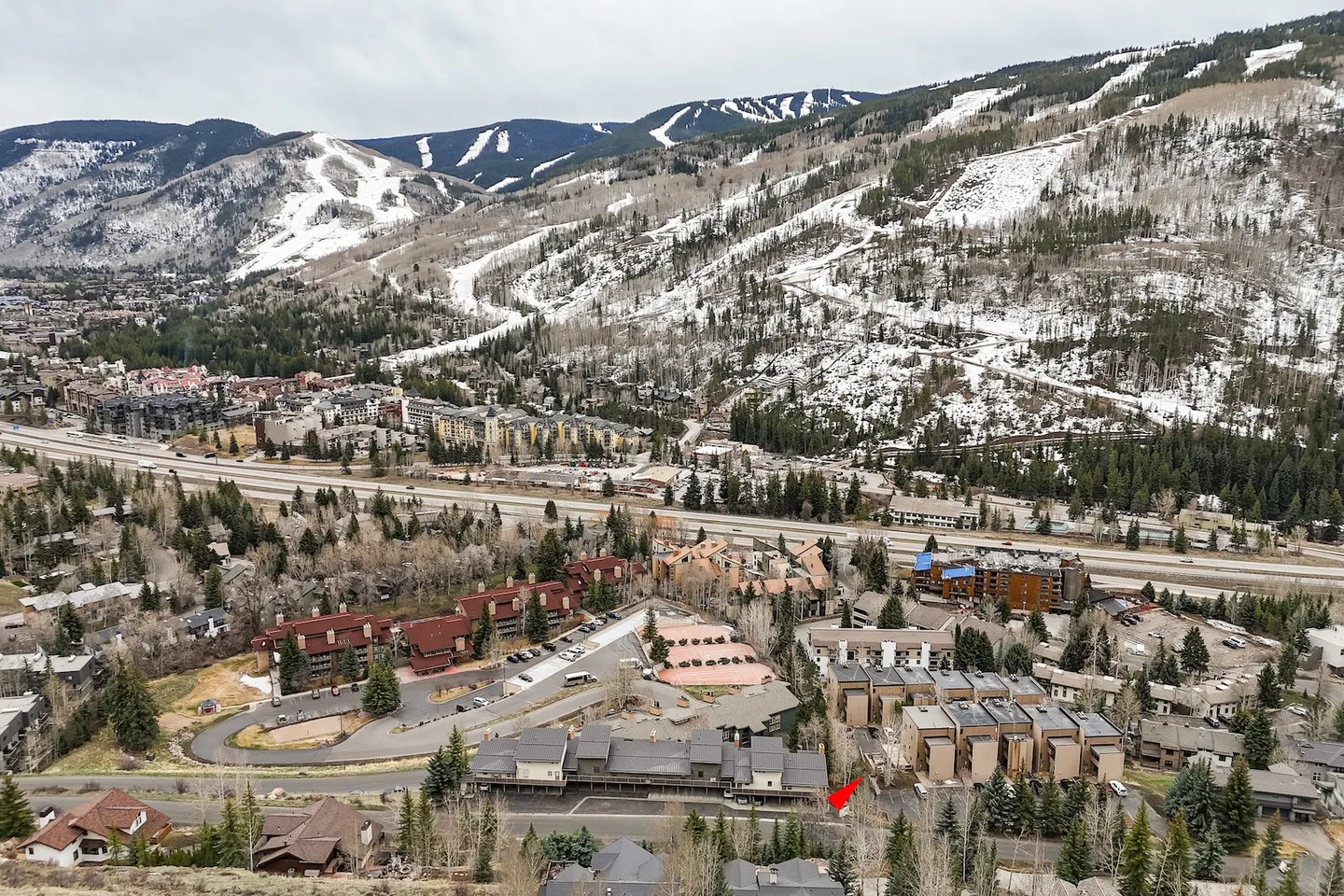 Aerial view of a mountain valley community with snow-dusted ski slopes and a red arrow marking a residential complex.