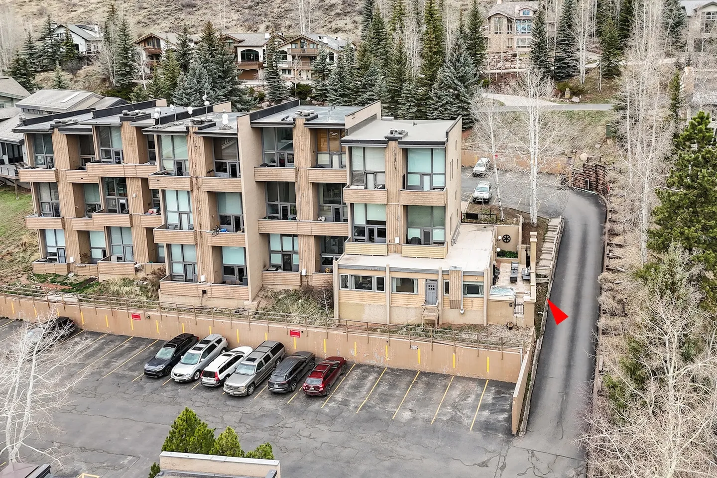 Elevated view of a multi-story modern residential condominium complex with an adjacent parking lot and access driveway surrounded by trees.