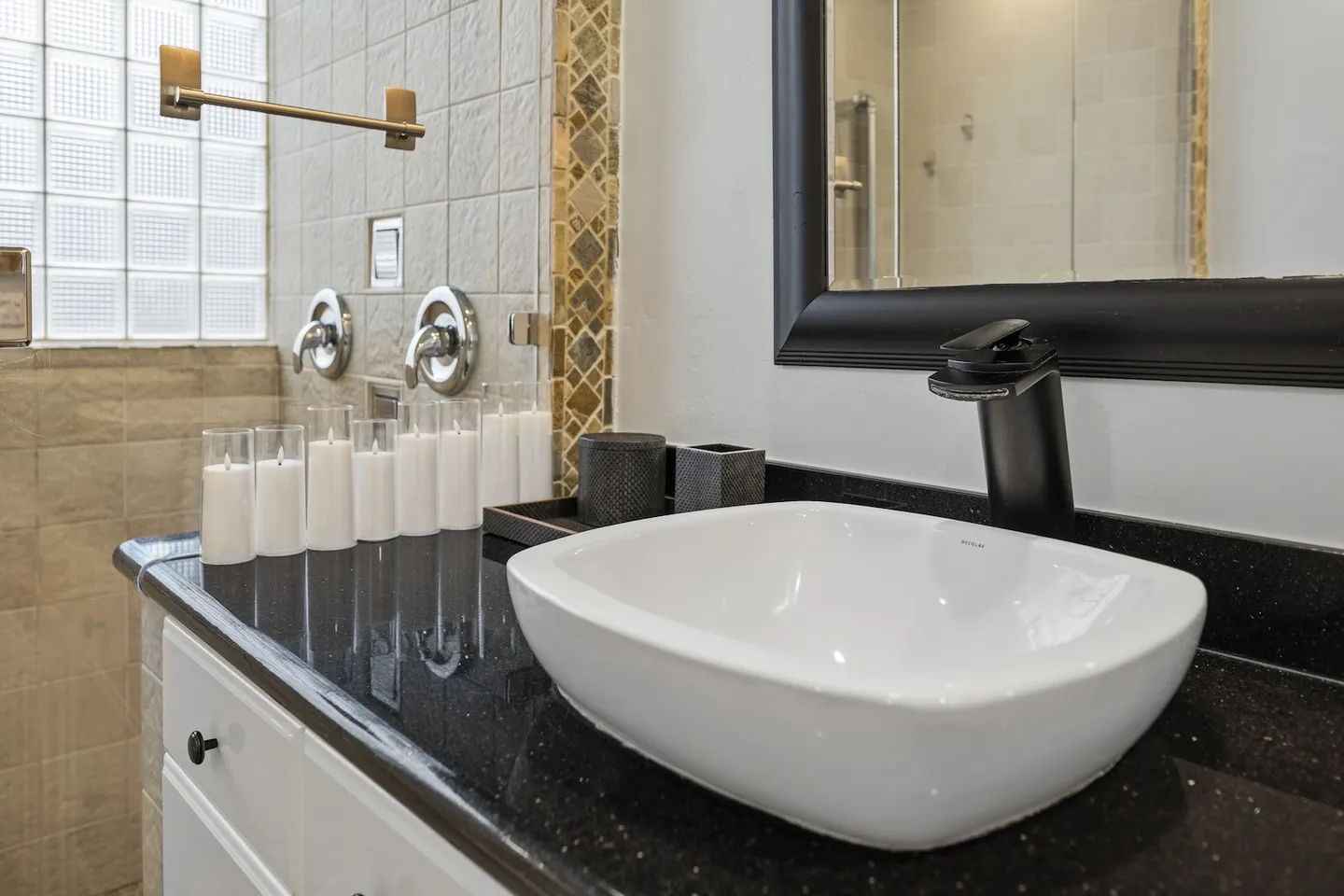 Bathroom vanity with a white vessel sink, black faucet, dark countertop, and decorative white candles.