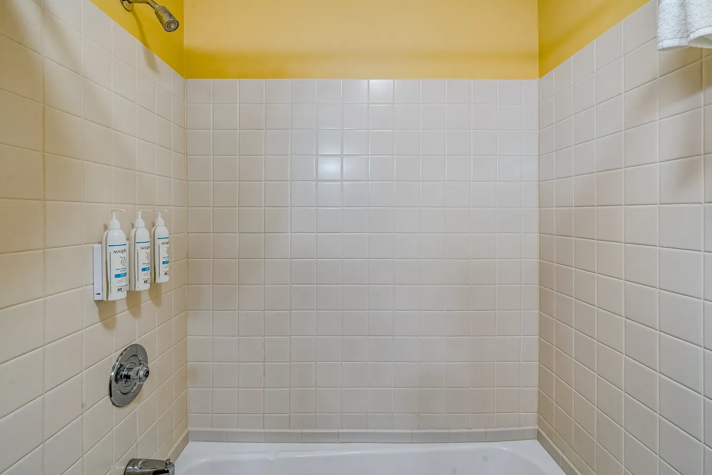 Bathtub and shower surround with square white tiles and yellow upper walls.