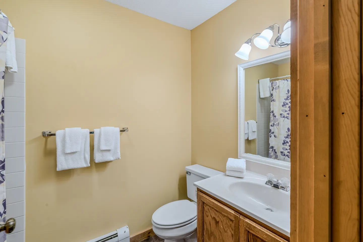 Bathroom featuring a vanity with a white framed mirror, a toilet, a towel bar with folded towels, and yellow walls.