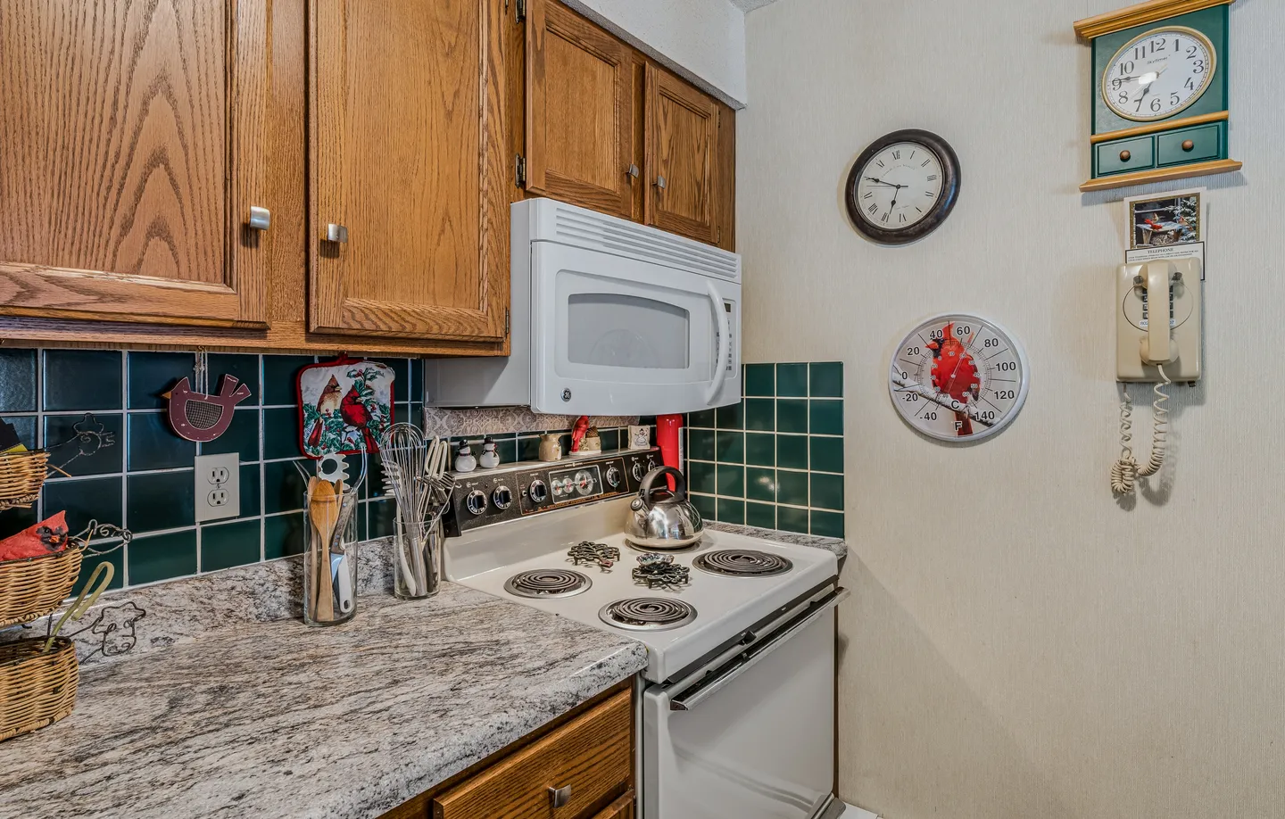 Kitchen counter and cooking area with oak cabinets, white microwave, white electric stove, dark green tile backsplash, and wall decorations.