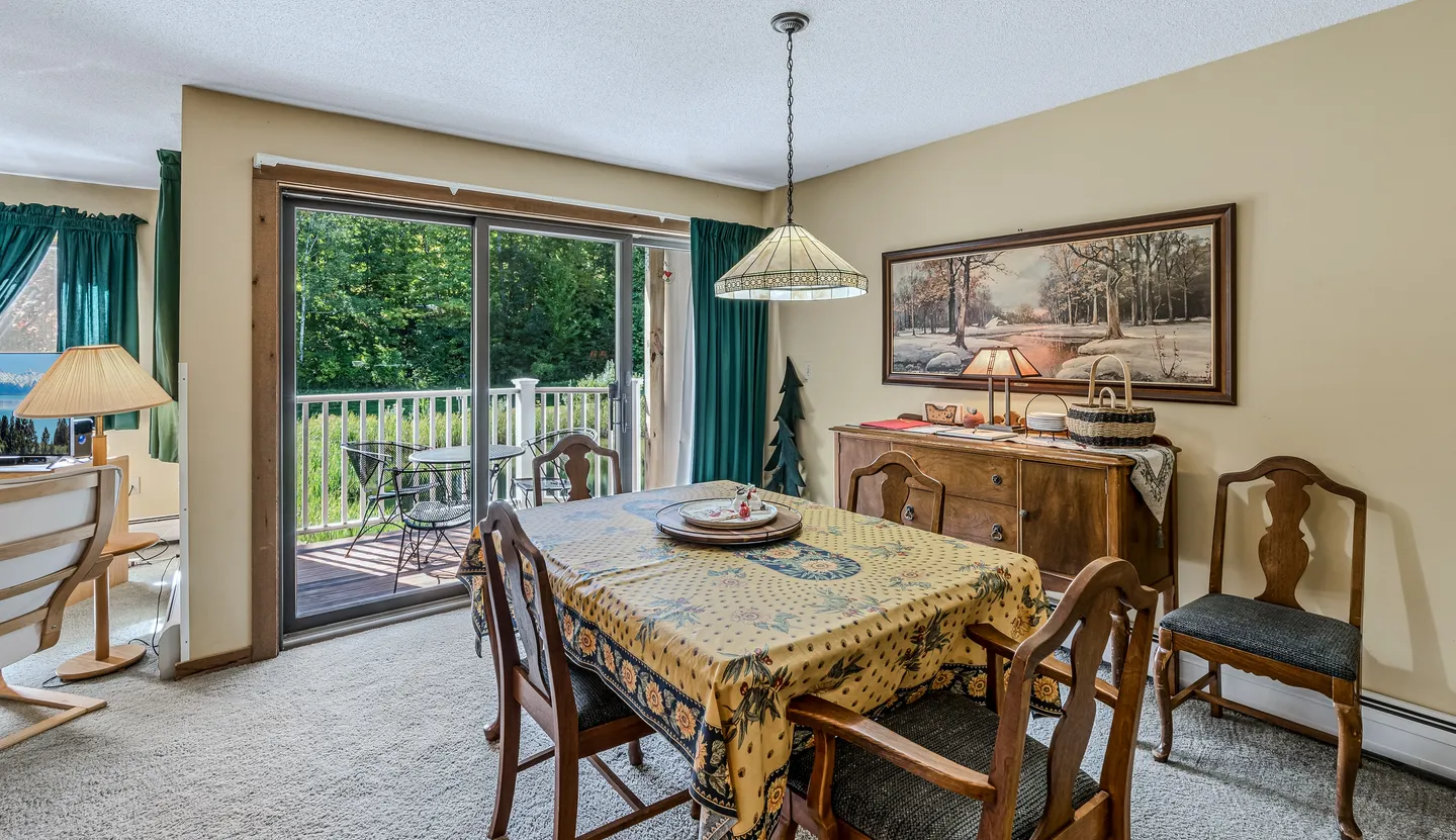 Dining area with a patterned tablecloth on the table, wooden chairs, a hanging pendant lamp, and sliding glass doors leading to a balcony.