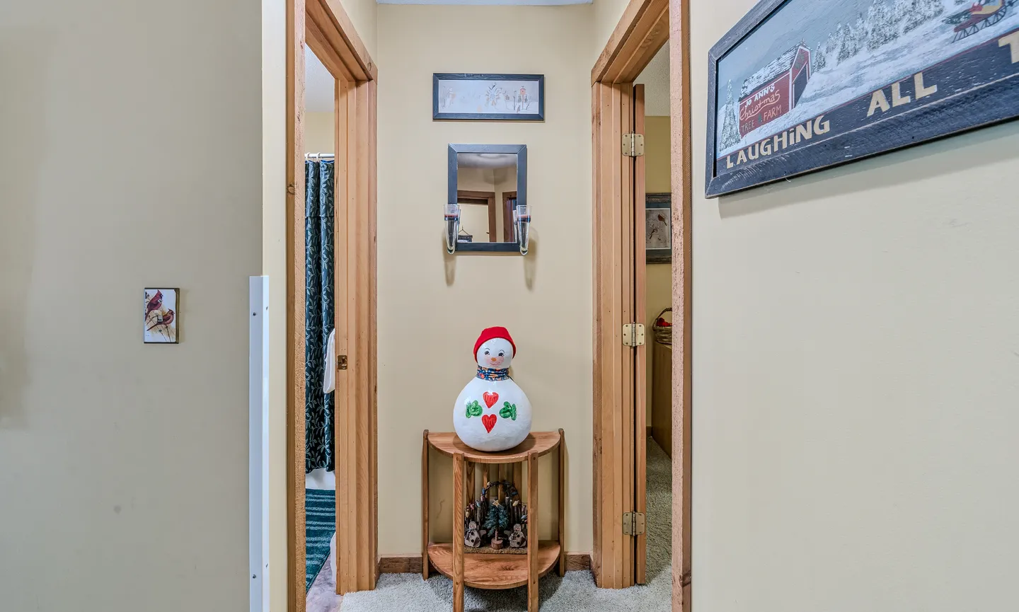 Hallway featuring beige walls, carpet flooring, a small corner table with a decorative snowman, and doorways leading to adjacent rooms.