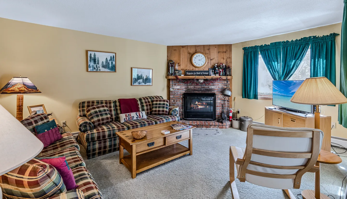 Living room with plaid sofas, a wooden coffee table, a corner brick fireplace, and a television on a console.