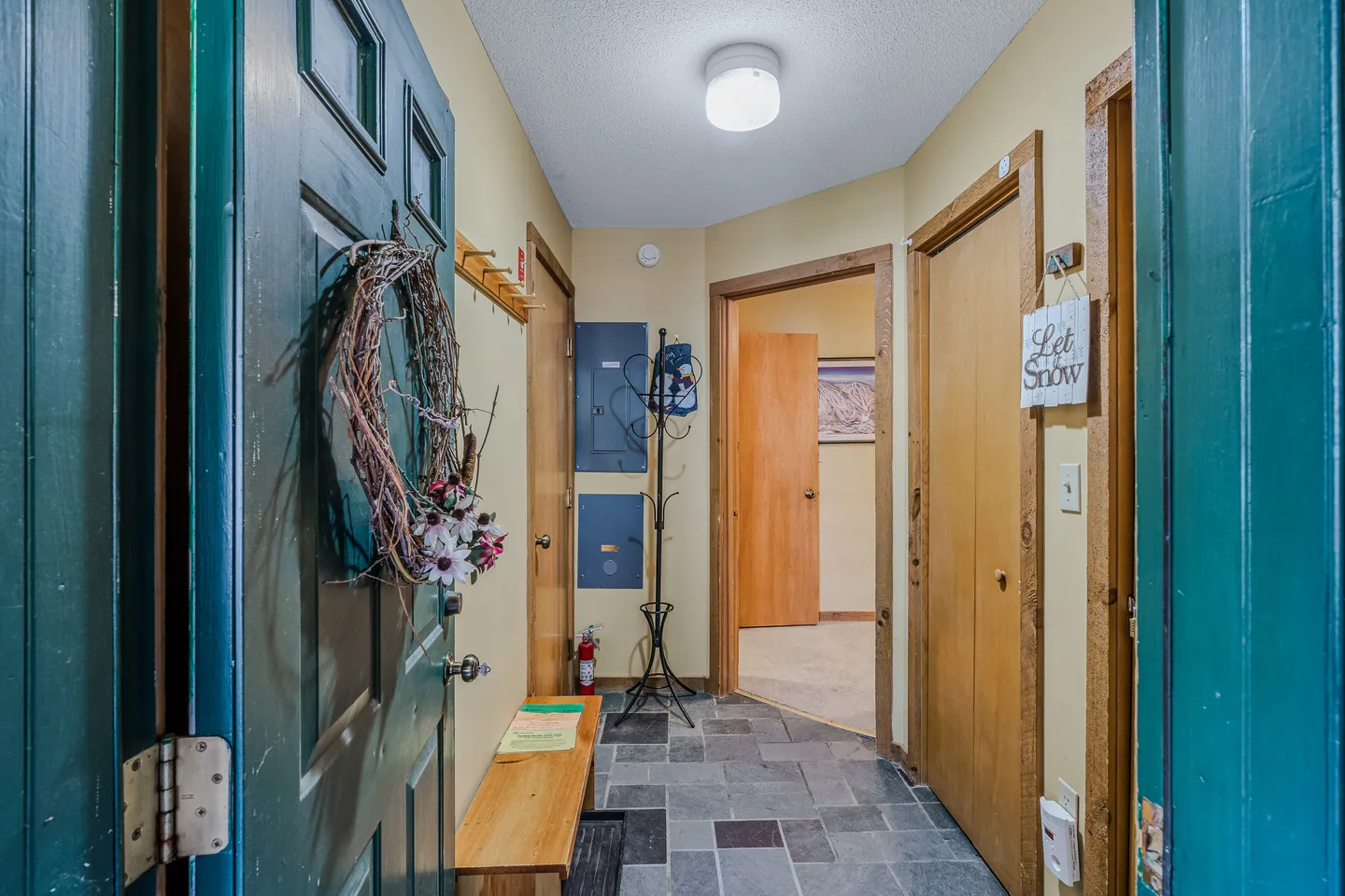 Entryway with dark slate-style tile flooring, wooden doors, a coat rack, and a green front door decorated with a wreath.