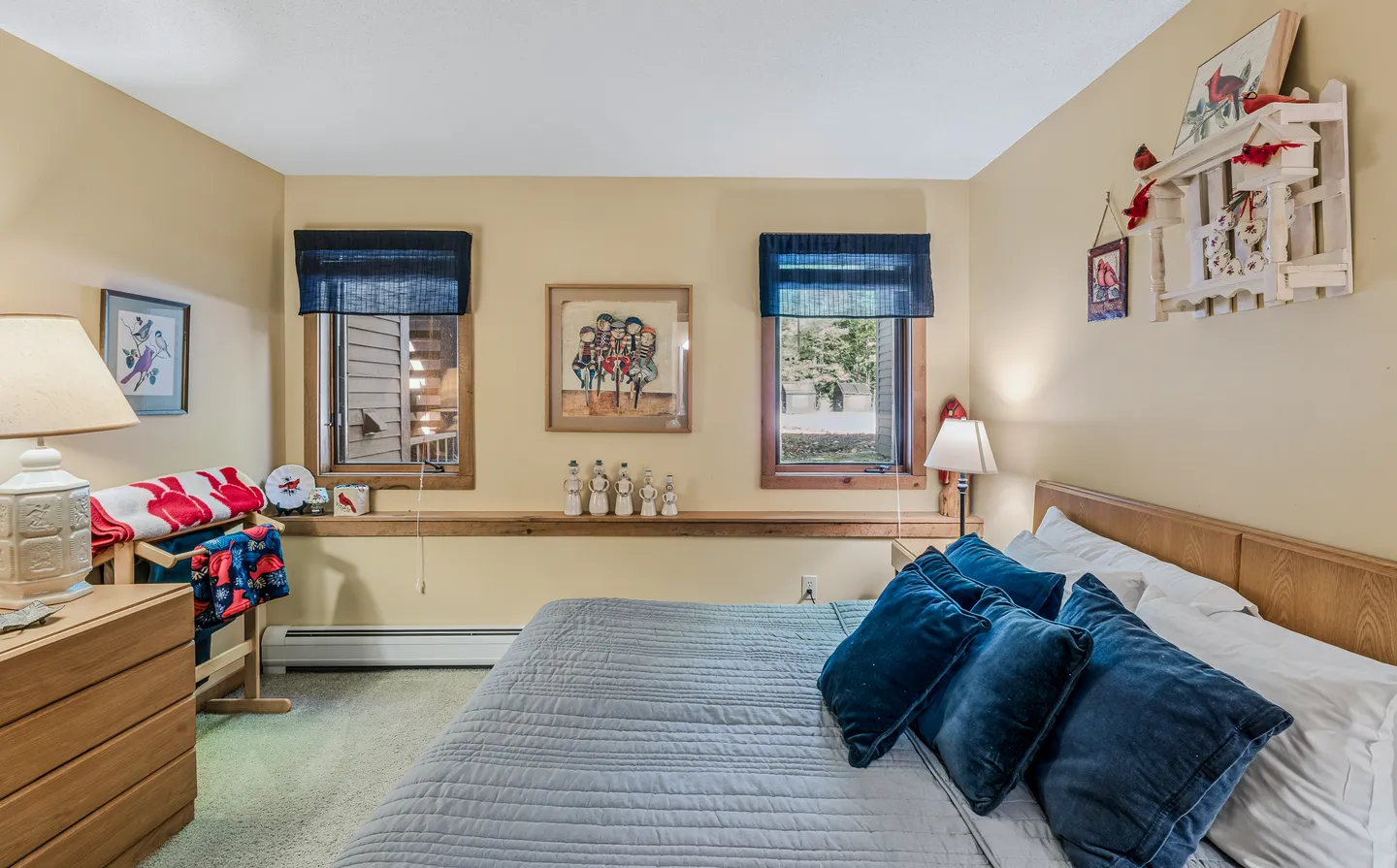 Bedroom with yellow walls, a wooden headboard, blue throw pillows, two windows with blue valances, and a wood ledge shelf.