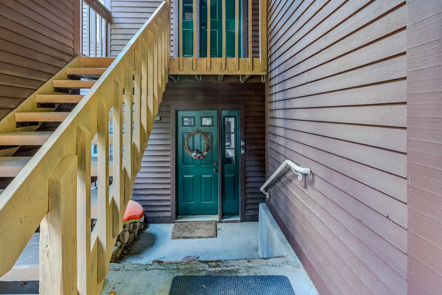 Exterior entryway with a dark green front door, a wreath, adjacent wooden staircase, and brown siding.