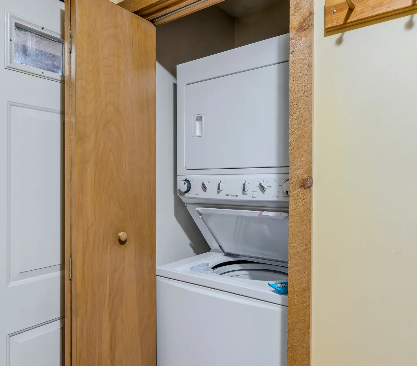 Stacked white washer and dryer unit inside a closet with an open wooden bi-fold door.