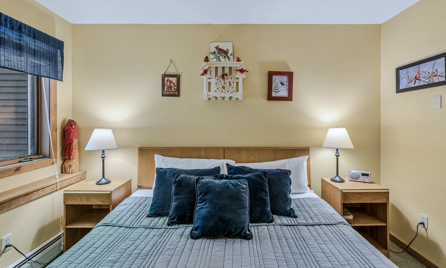 Bedroom featuring a made bed with navy blue and gray bedding flanked by matching wooden nightstands with glowing table lamps.