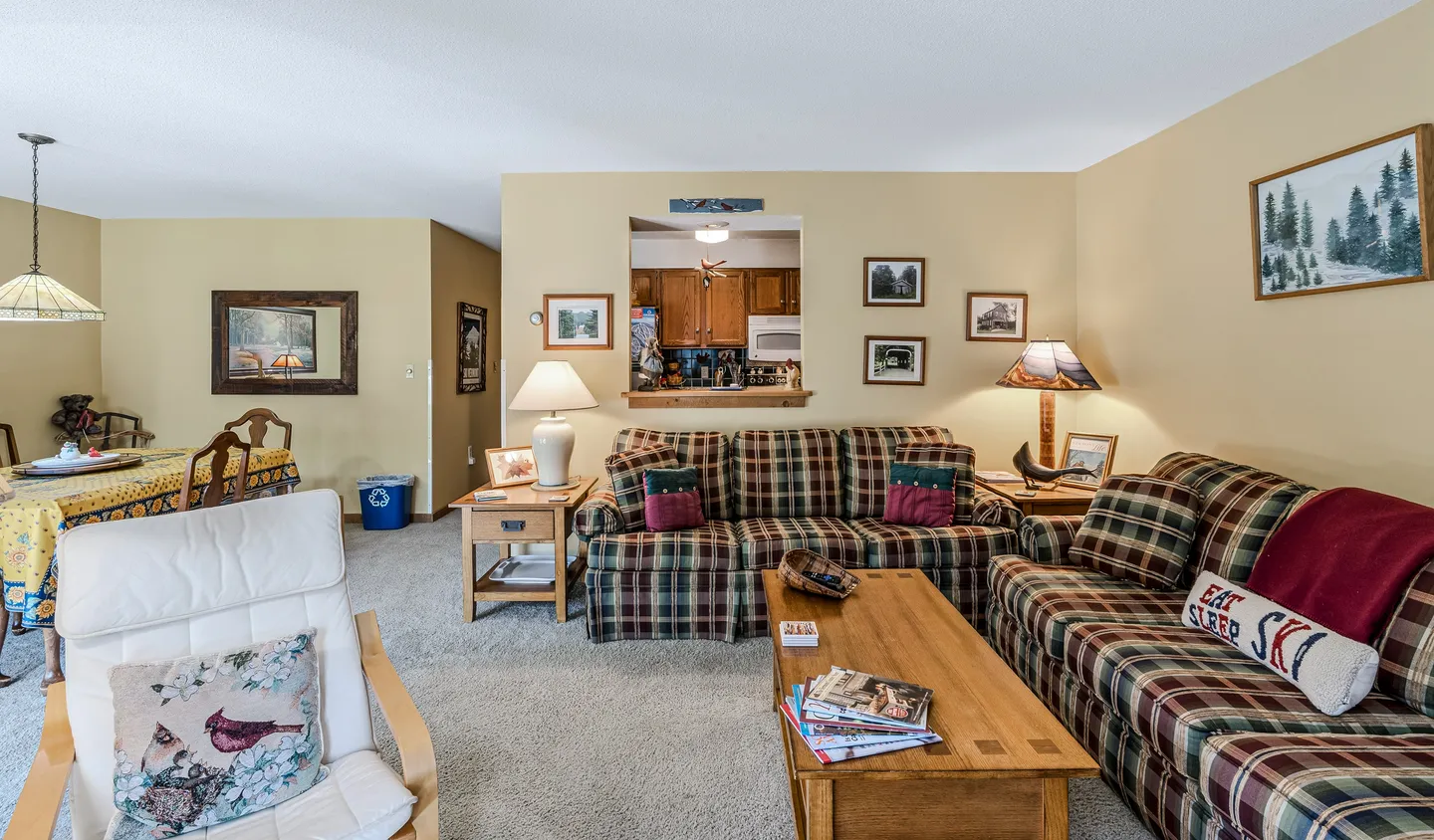 Living room with plaid sofas, wooden coffee table, white armchair, and a pass-through window into the kitchen.