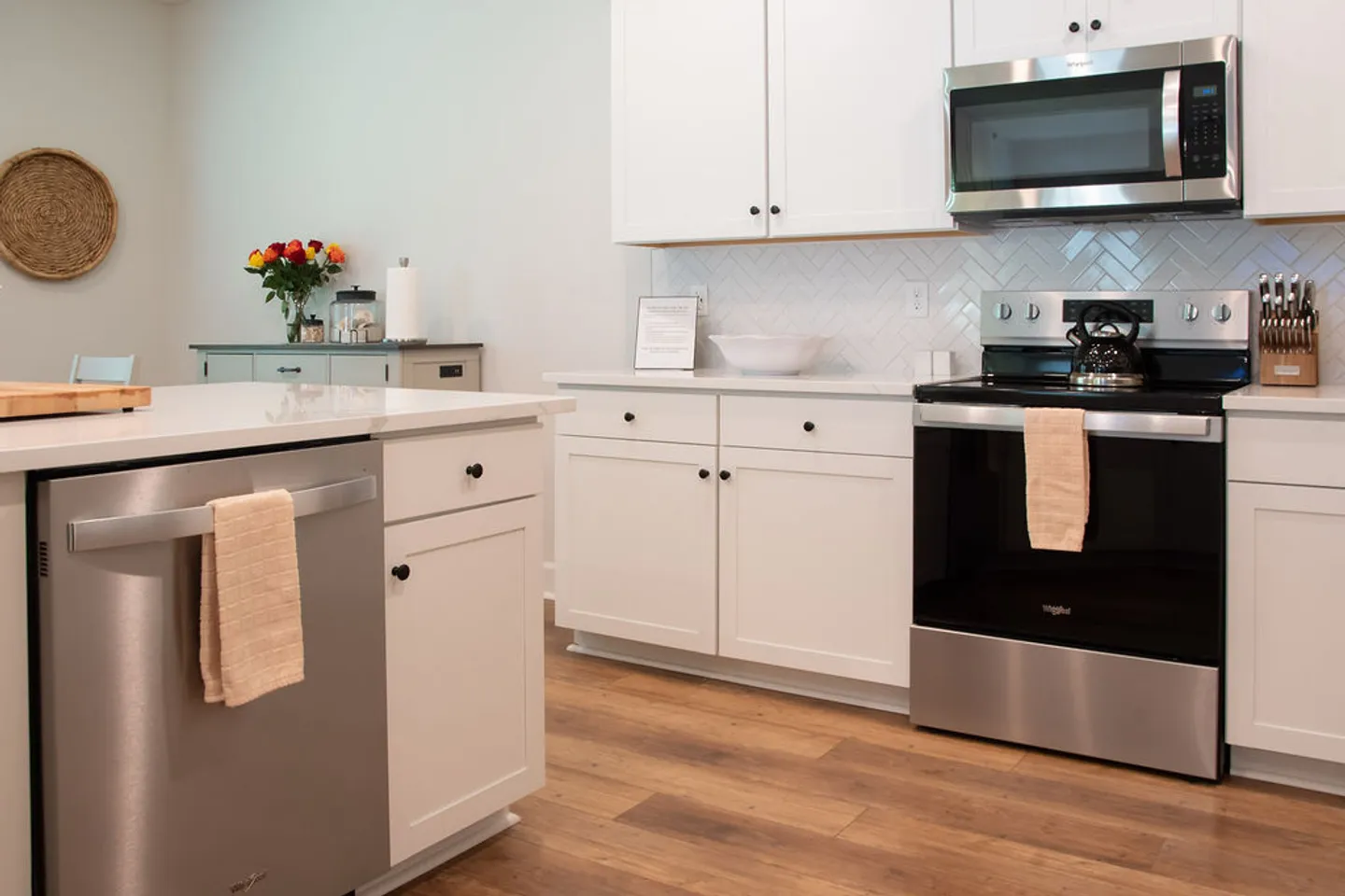 Kitchen interior featuring white cabinetry, wood-style flooring, and stainless steel appliances including a dishwasher, range, and microwave.