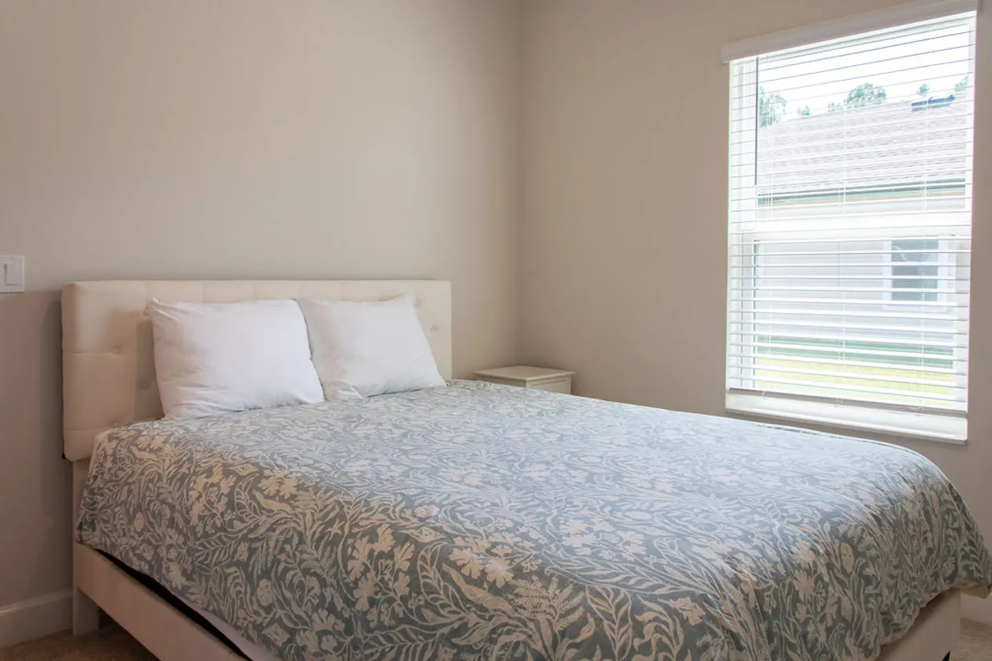 Bedroom with a bed featuring an upholstered headboard, patterned blue and white duvet, and a window with horizontal blinds.