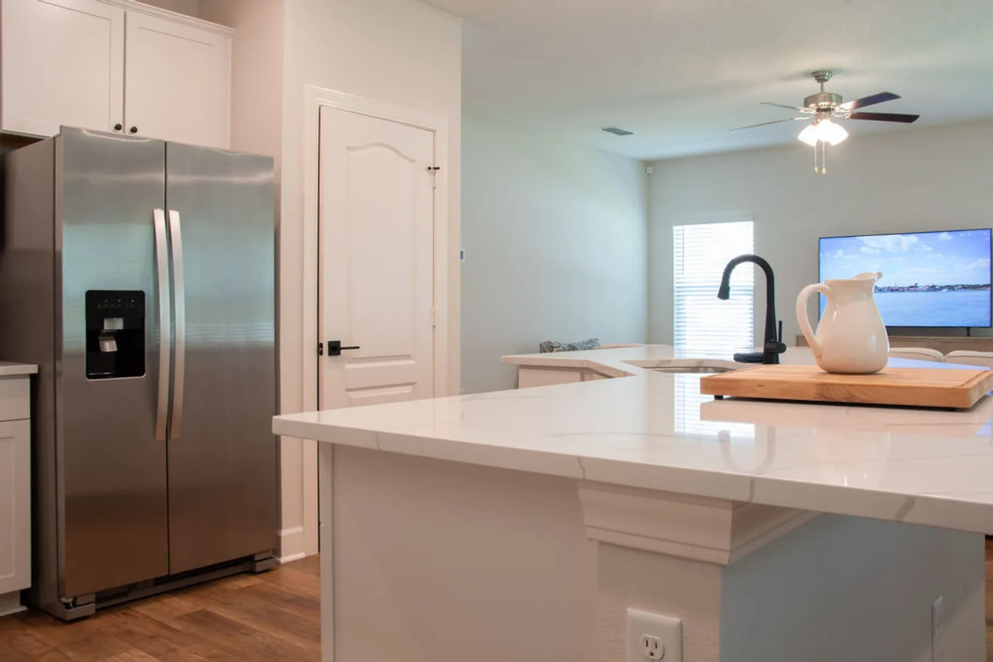Kitchen island with marble-look counter and black faucet overlooking the living room and stainless steel refrigerator.