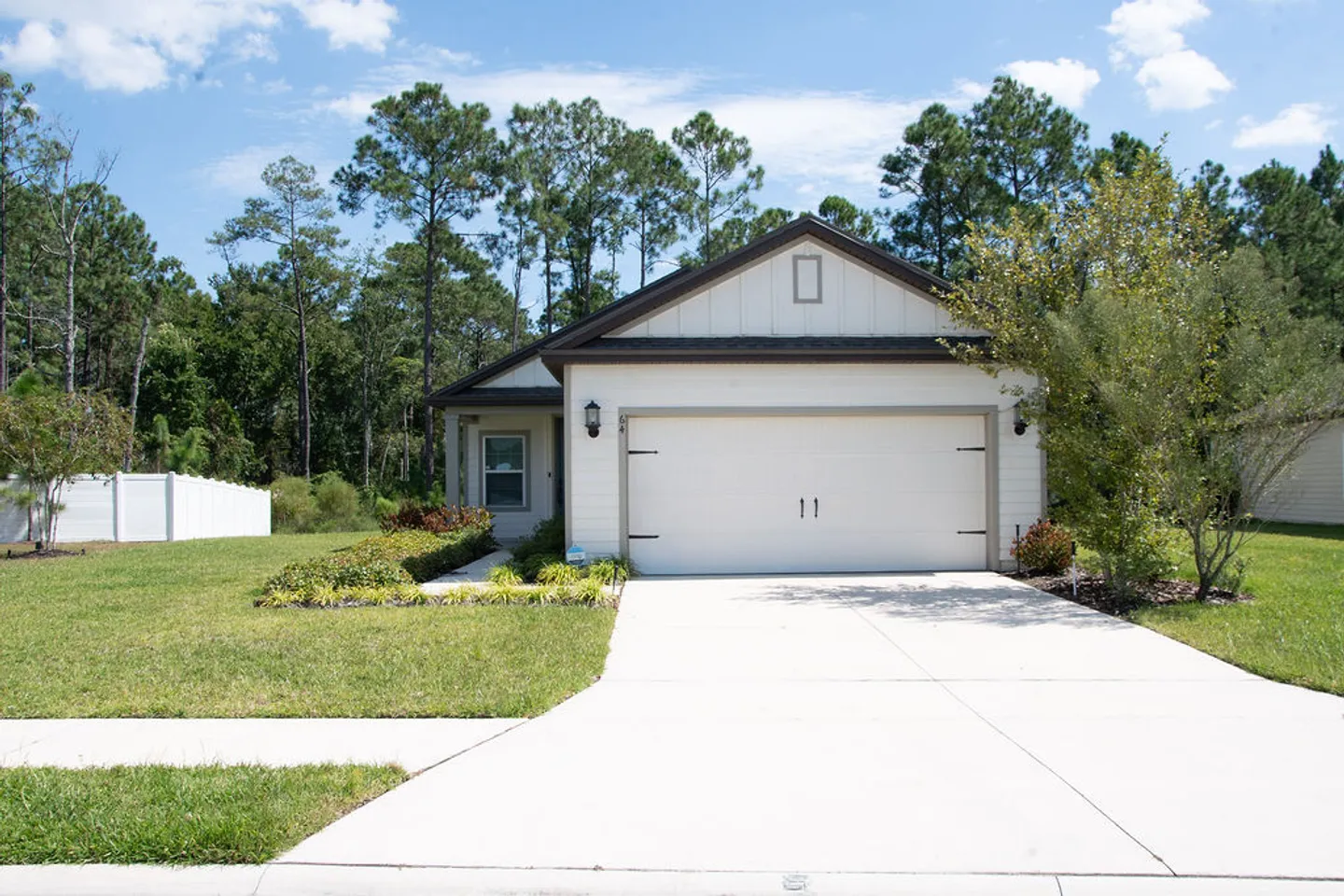 Front exterior of a single-story house with a two-car garage, concrete driveway, and front lawn framed by trees.