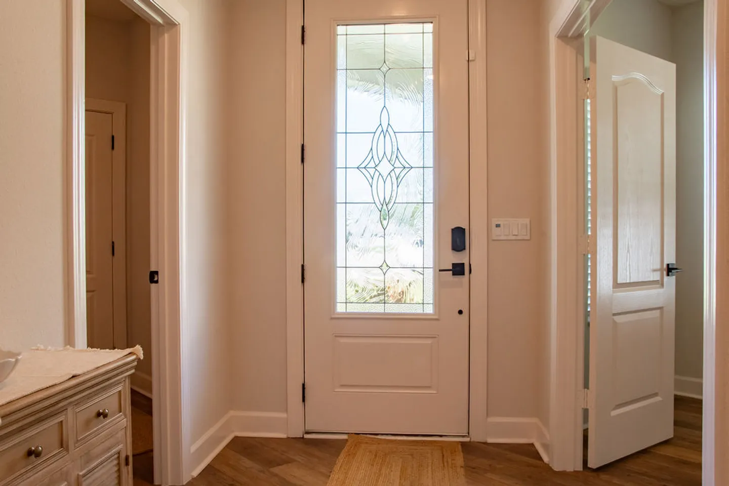 Front entryway with a white door featuring a frosted decorative glass insert, wood-look flooring, and doors on either side.
