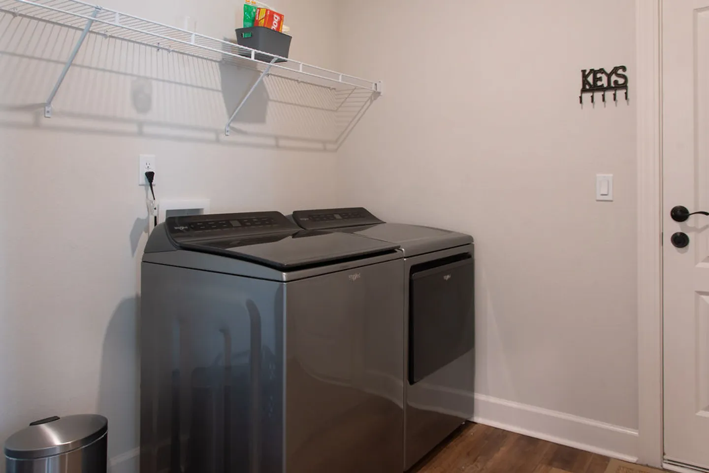A laundry room area with a gray matching washer and dryer set beneath a wire shelf.
