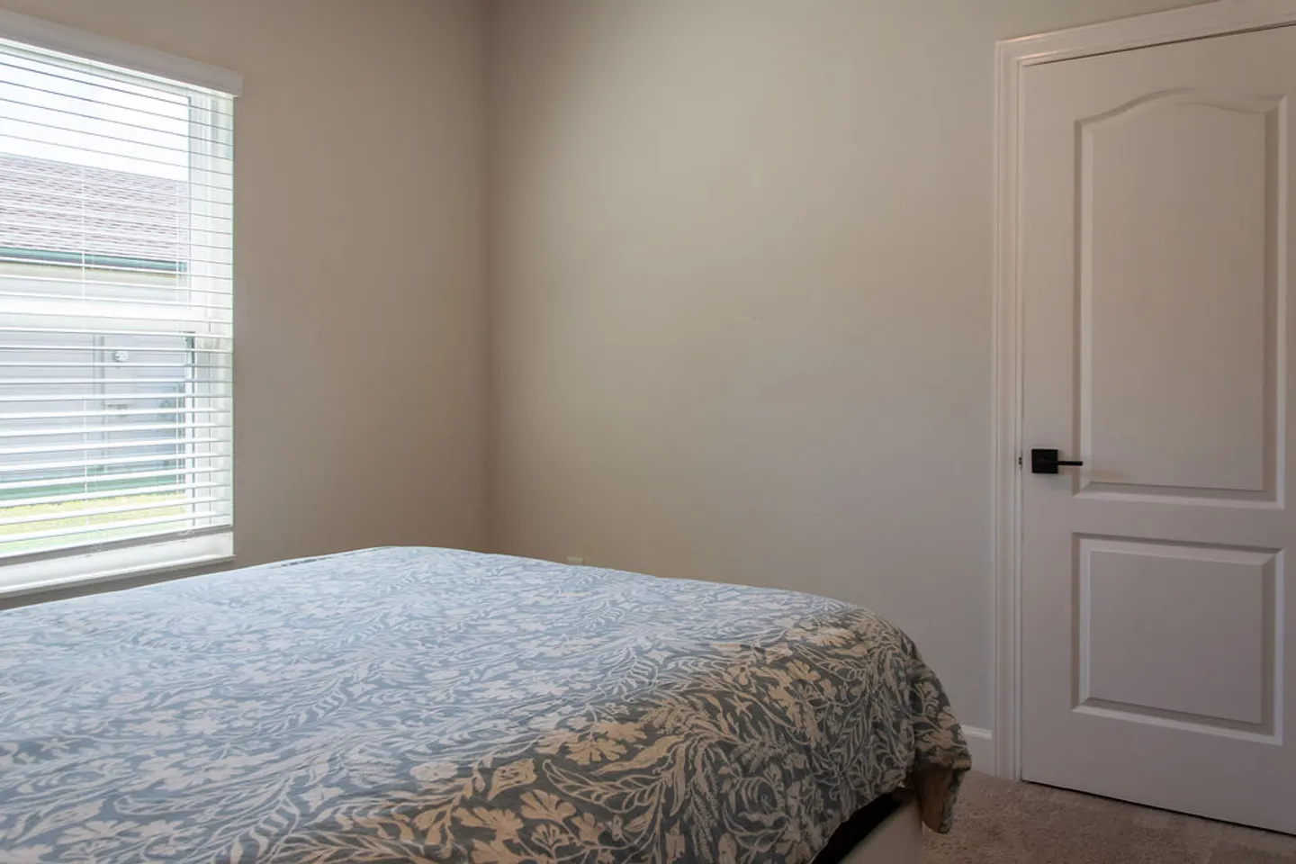 Bedroom featuring a bed with a blue and white patterned duvet, a window with horizontal blinds, and a white interior door.