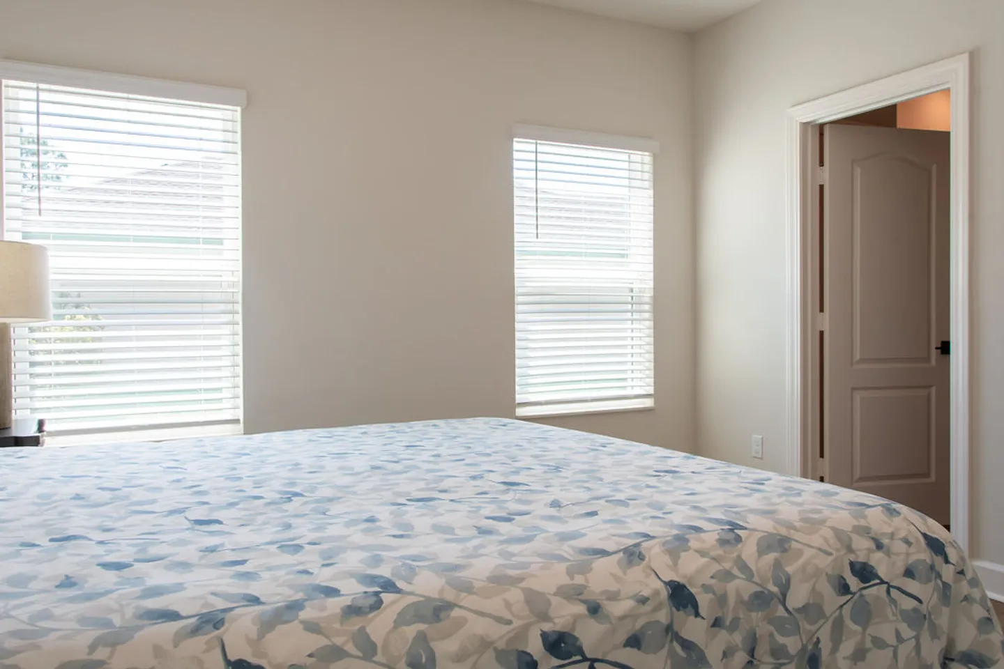 Bedroom featuring a bed with a blue and white patterned comforter, two windows with horizontal blinds, and an open interior door.