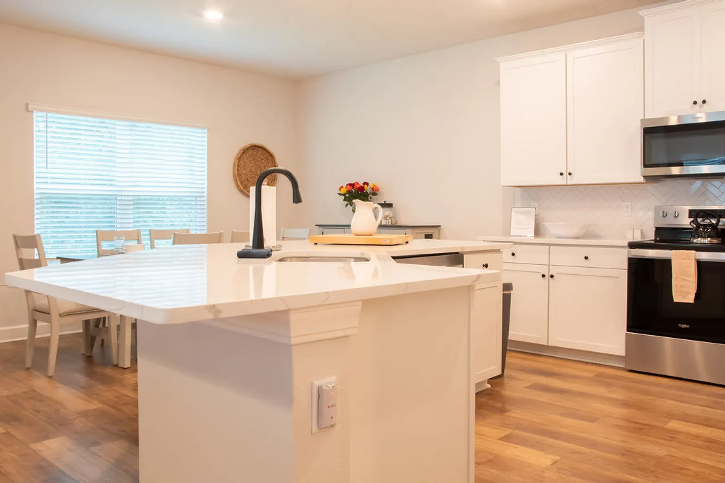 Bright kitchen featuring a white island with a dark faucet, white shaker cabinetry, stainless steel appliances, and wood-look flooring.