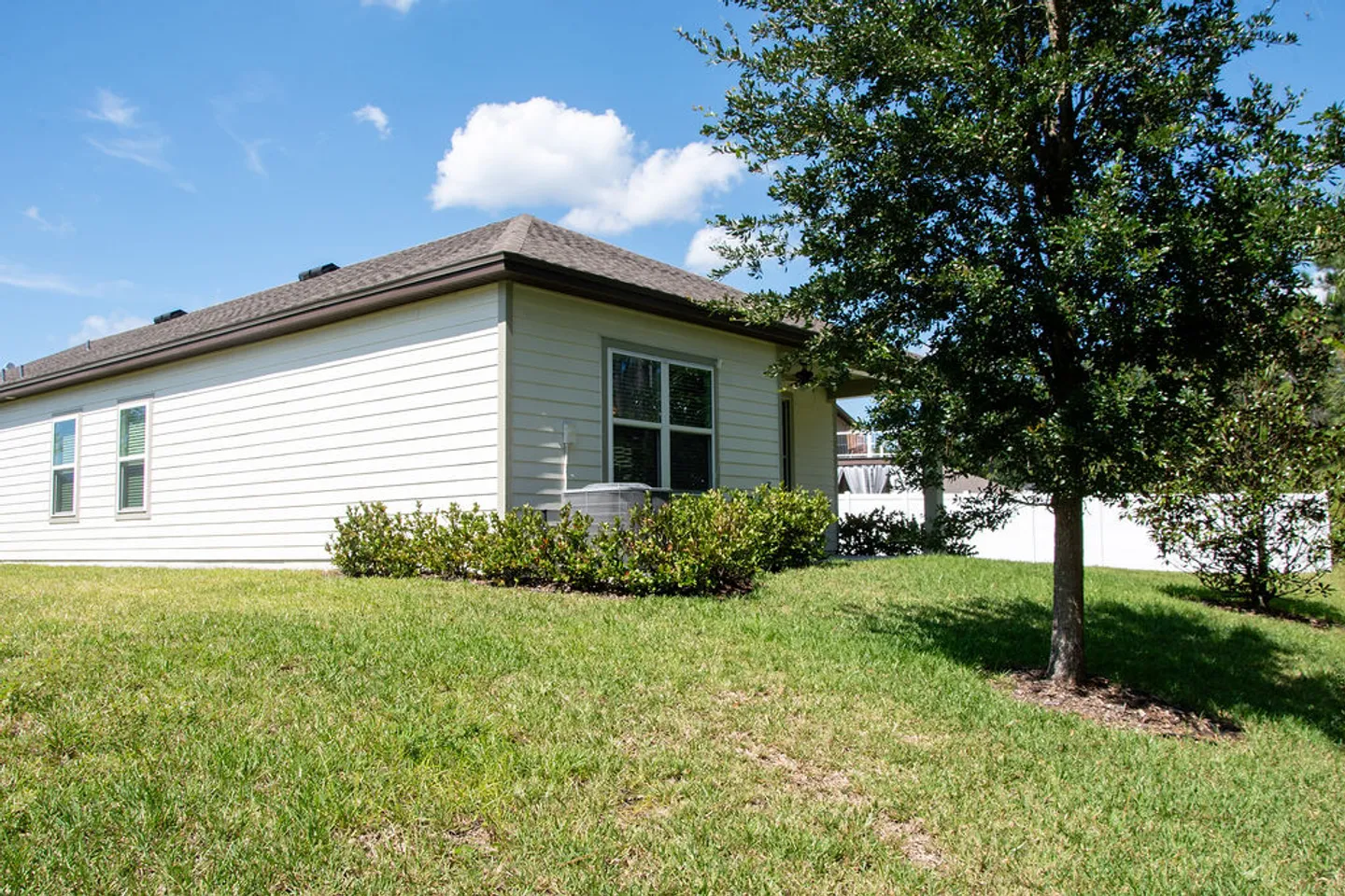 Exterior view of the side and back of a single-story home with white horizontal siding and a grassy lawn under a blue sky.