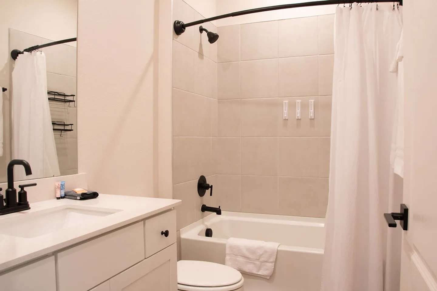 Bathroom with white vanity, toilet, and tiled shower-tub combination featuring matte black fixtures.
