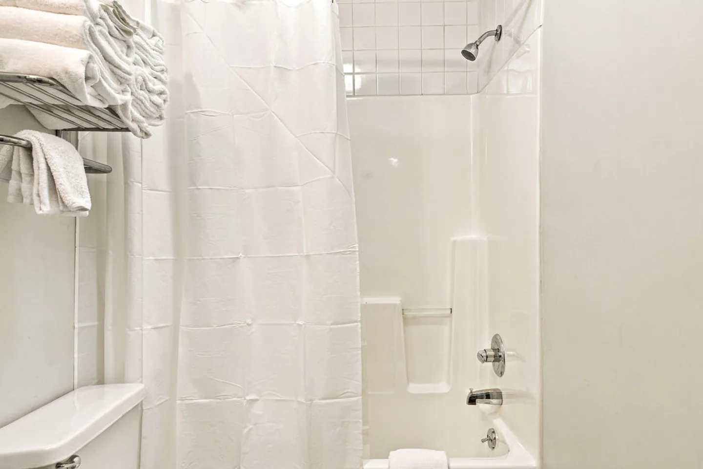Bathroom with a combined shower and bathtub, white shower curtain, and a wall-mounted metal towel rack.