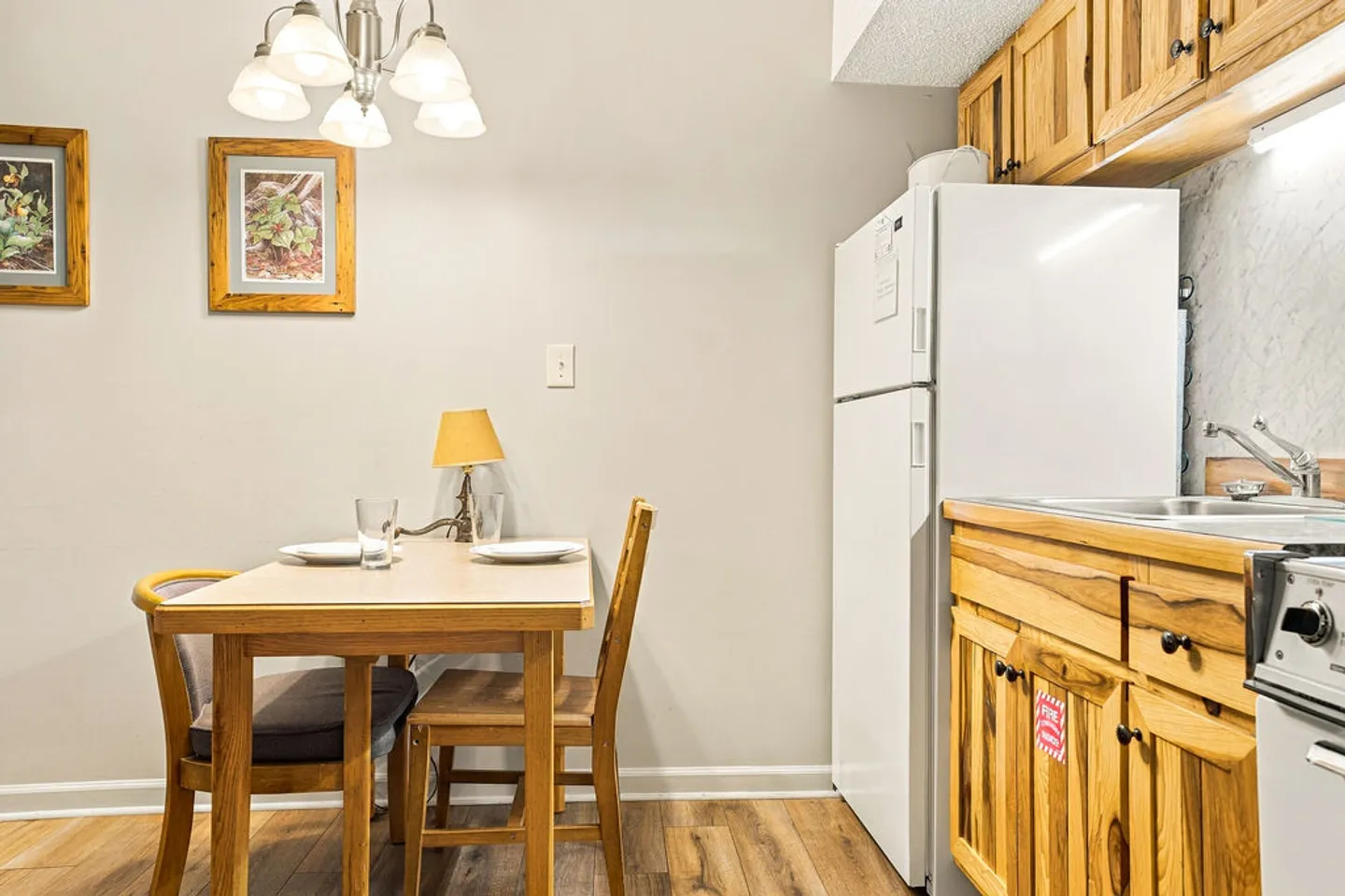 Dining table with chairs adjacent to a white refrigerator and kitchen cabinetry.