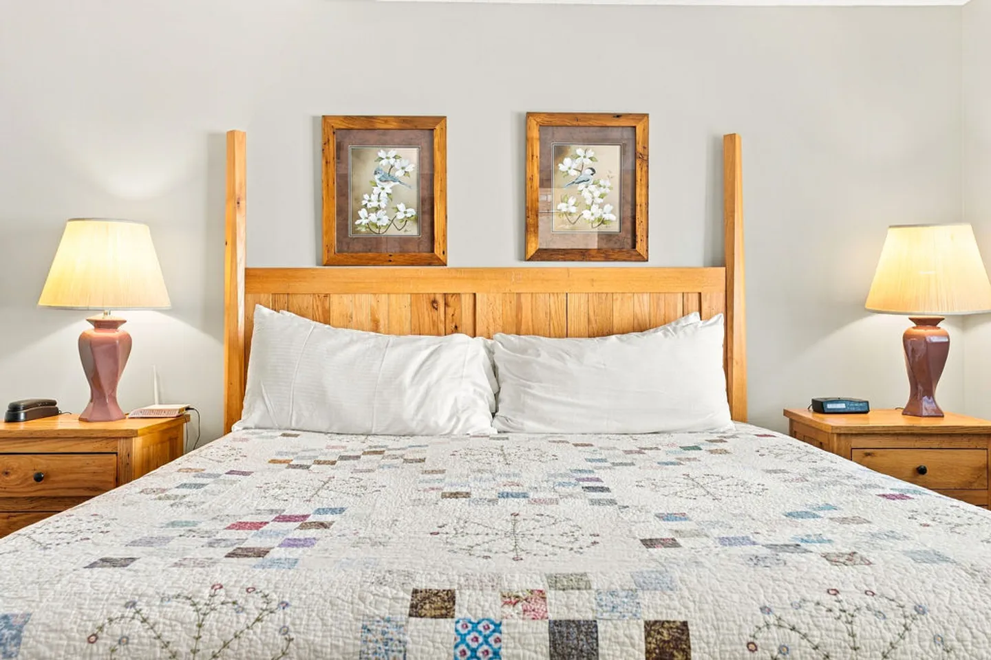 A made bed with a light-colored patchwork quilt and wooden headboard flanked by two matching nightstands and lamps.