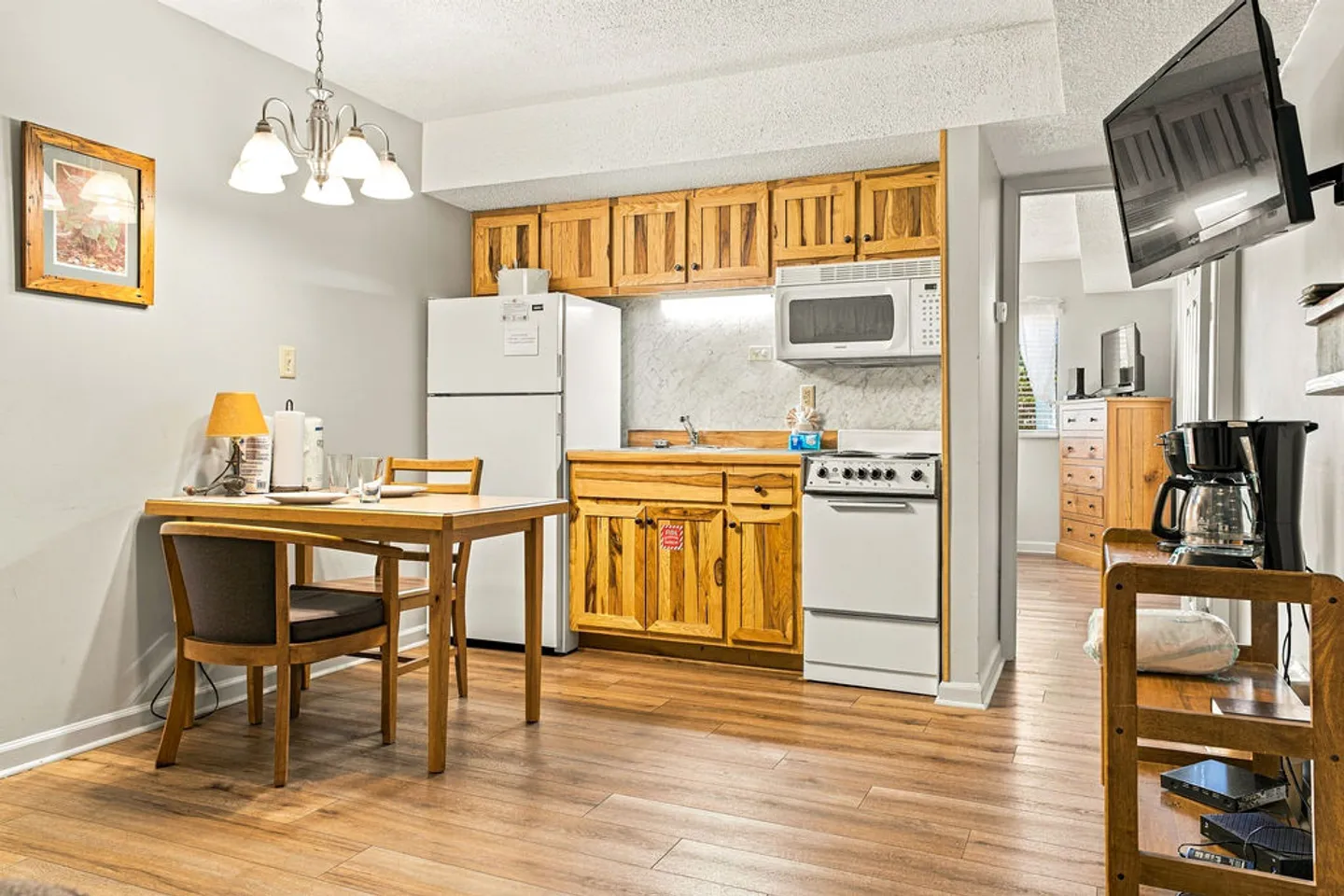 Kitchenette with wood cabinets, white appliances, and a dining table with chairs under a chandelier.