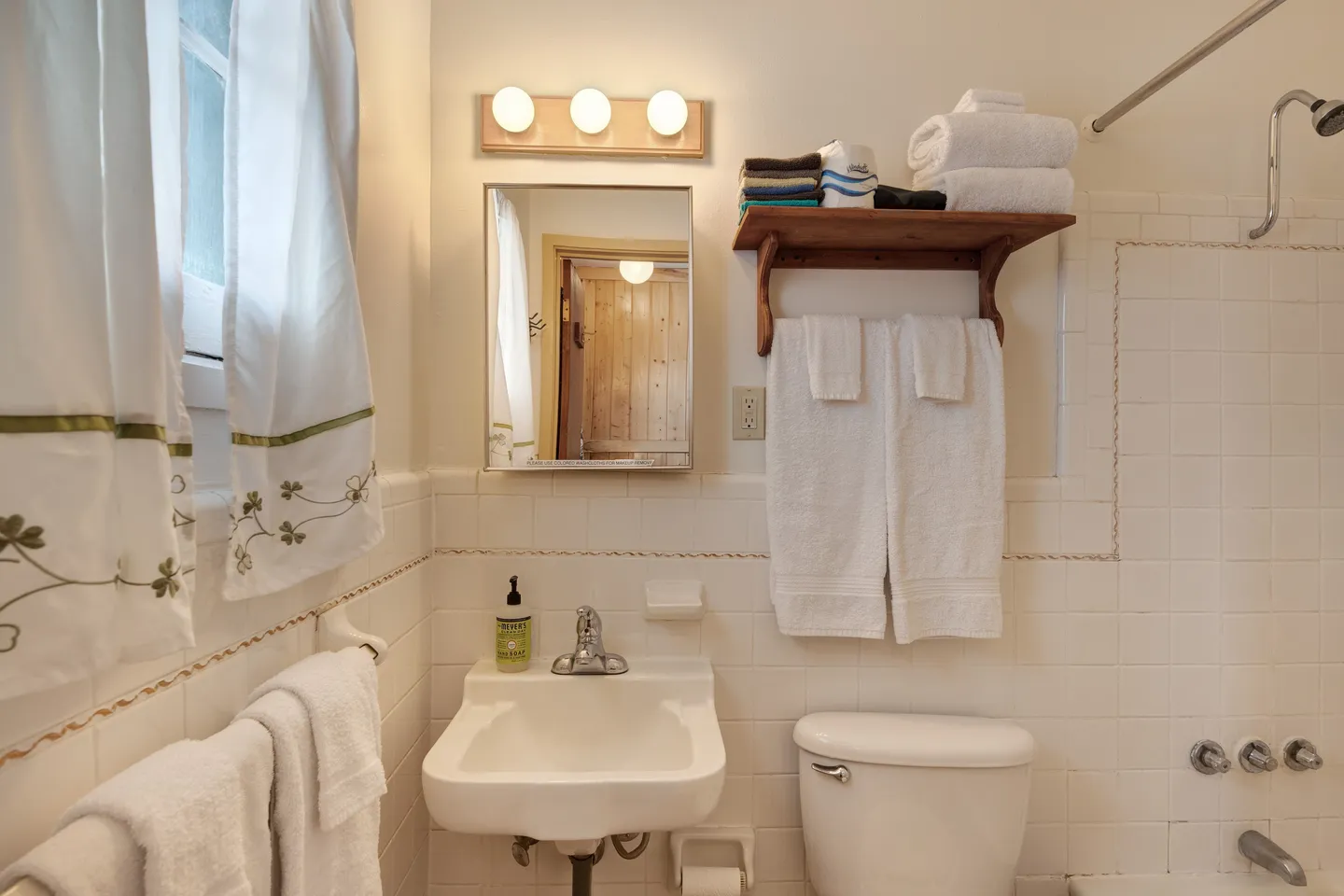 Bathroom with a wall-mounted sink, mirror with vanity lights, toilet, and tiled shower wall.